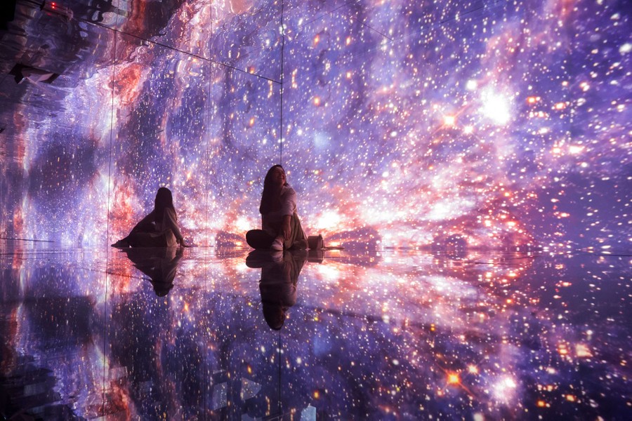 A person sits on the floor inside a mirrored room lit up with an image of stars.