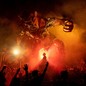 A crowd gathers in a street at night, around a giant sculpture of a demon, during a festival.