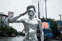 A street performer, with his body completely covered in silver paint, salutes while begging for money in a street.