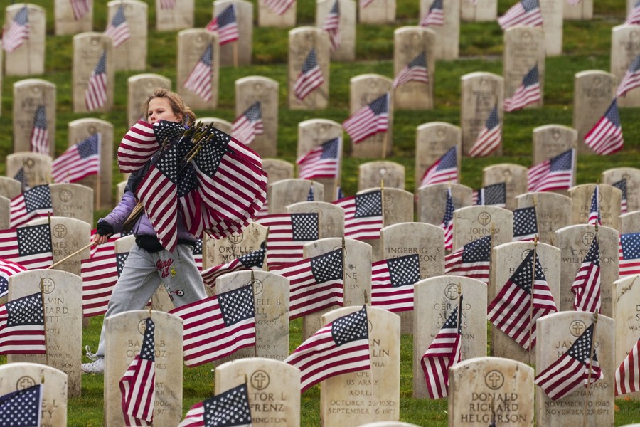 A child carries a bundle of American flags in a military section of a cemetery.
