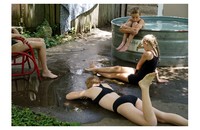 four kids sitting around outside in bathing suits, one sitting at the edge of a pool, two on the ground, one in a red chair