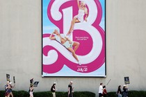 Strikers march beneath a poster for the 'Barbie' movie.