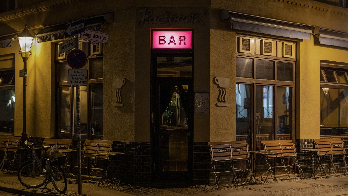 A bar at night, with an illuminated pink sign in the center and folded up tables along its windows