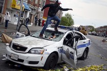 A man jumps on a destroyed Baltimore Police car during protests after the death of Freddie Gray.