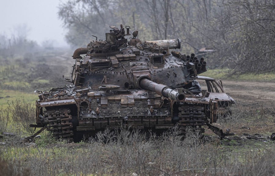 An abandoned and badly damaged tank sits in a field.