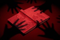 Shadowy hands reach for a book with a map of Europe on its cover
