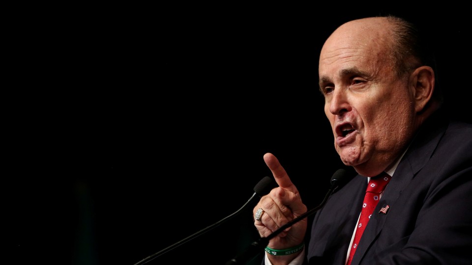 A close-up of Rudy Giuliani speaking on a stage in front of a black backdrop