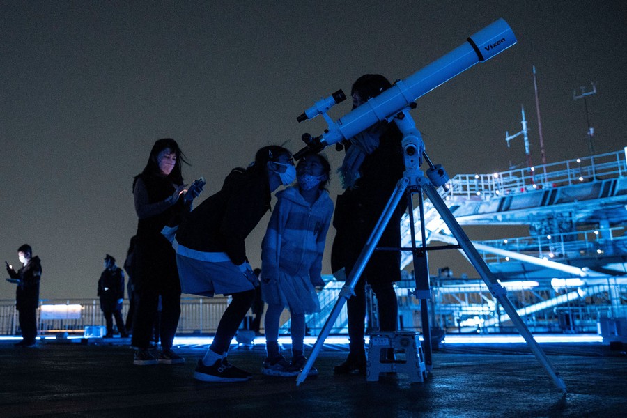 Several people gather and look through a telescope.