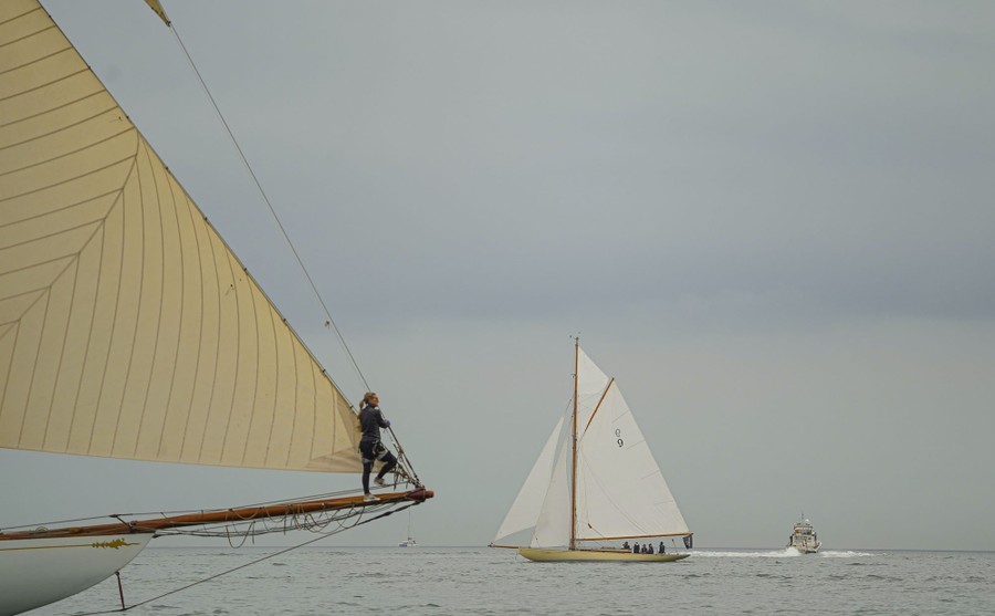 A person stands at the very end of a beam at the bow of a large sailboat.