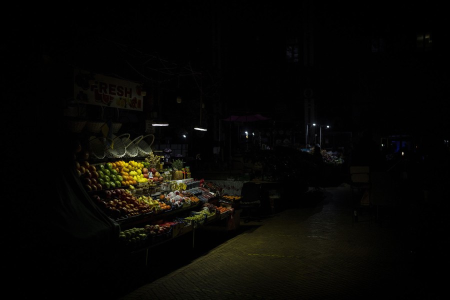 A fruit stand is lit by two small lamps on a very dark street.