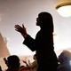 Two Black women stand in a church among other parishioners.