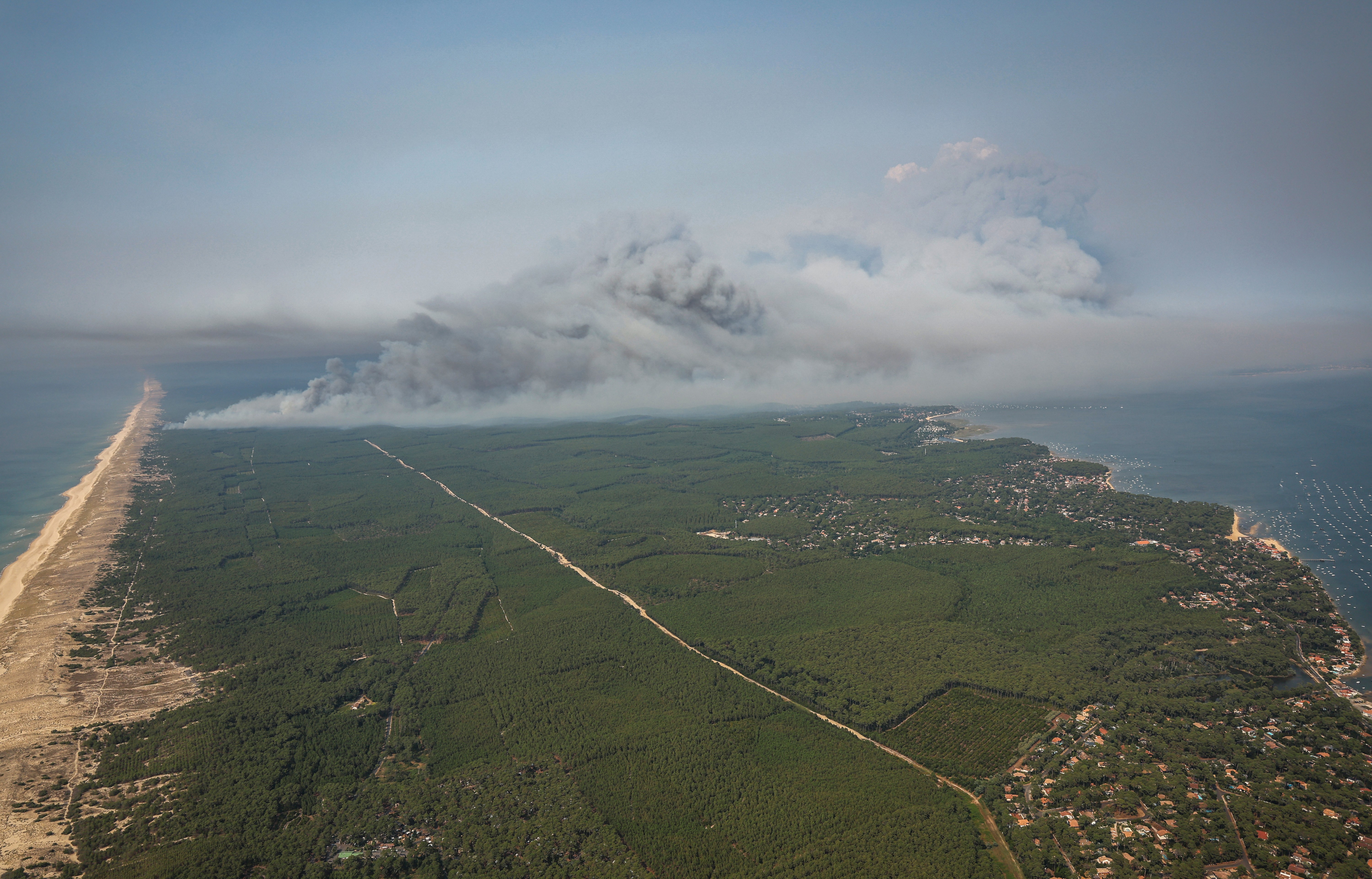 An aerial photograph showing smoke rising from a wildfire near a coastline.