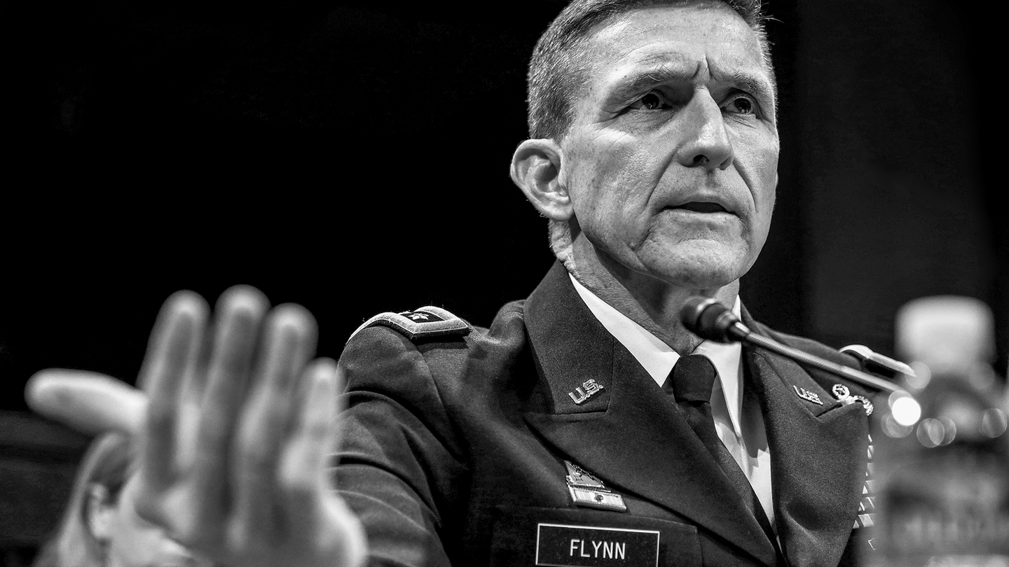 Fotografía en blanco y negro de Michael Flynn en uniforme testificando ante el Congreso con un micrófono.