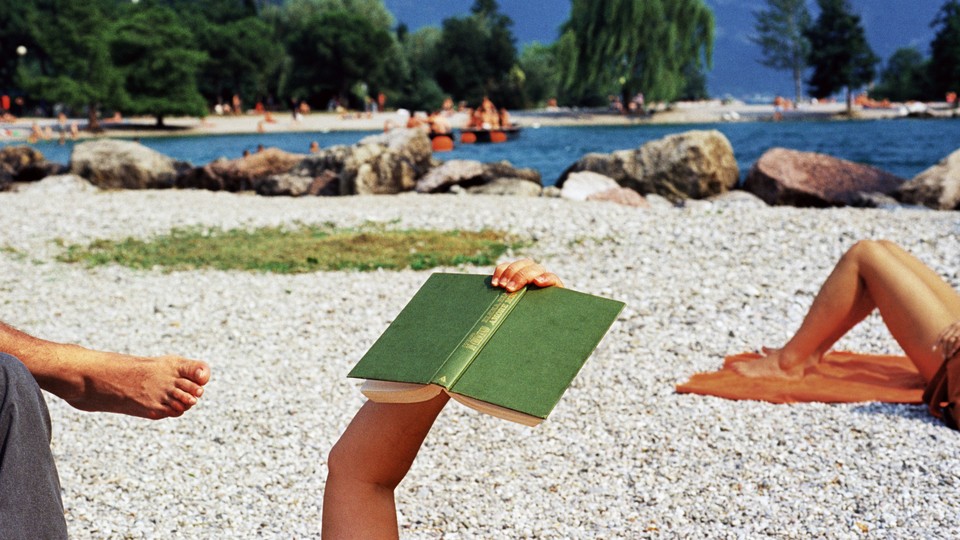 A photo of a person reading outdoors on a beach.