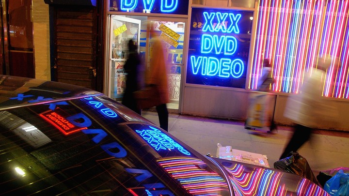 The neon lights of an adult-video store are reflected on a car.
