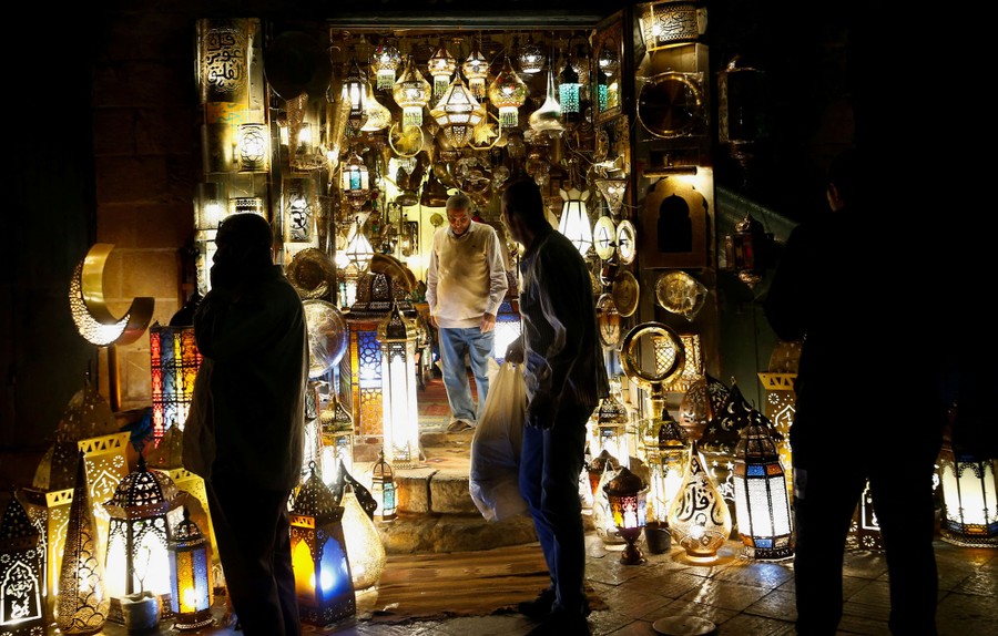 People walk past a storefront lit by traditional lanterns.