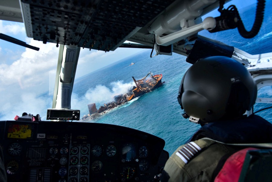 A view from an aircraft interior, showing a burning cargo ship seen through the front windows.