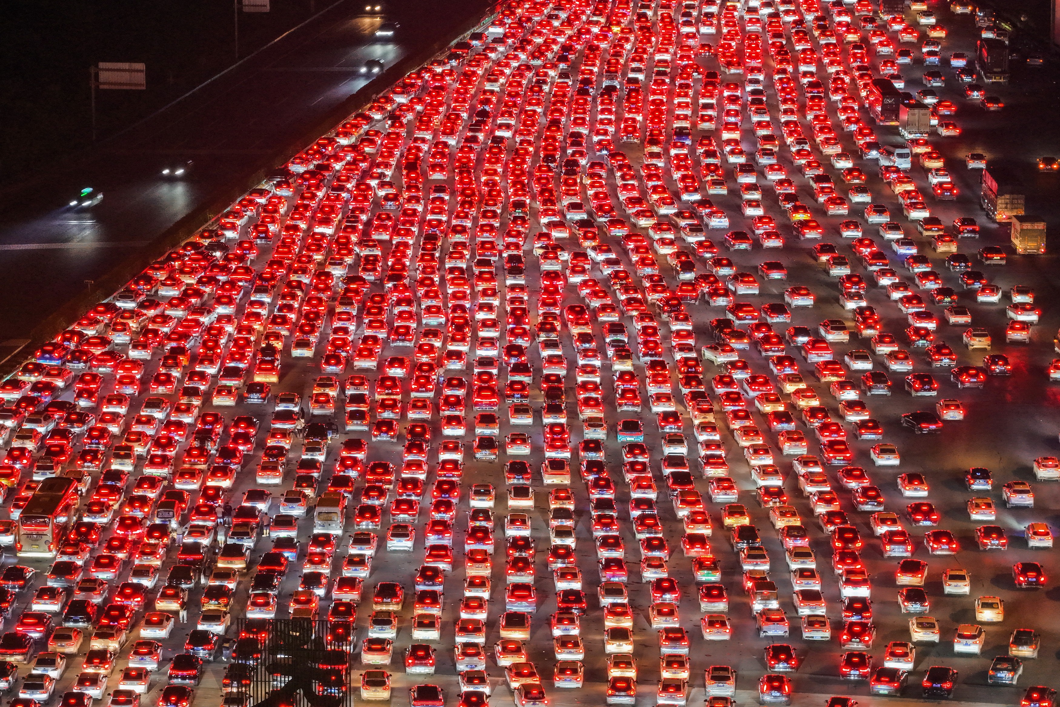 Hundreds of cars merge from several dozen lanes down to just a few, seen from above, a sea of red brake lights.