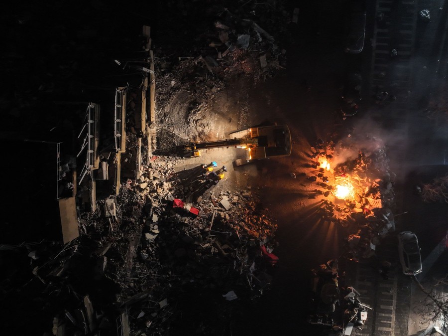 An aerial view of people gathered around a fire beside a collapsed building