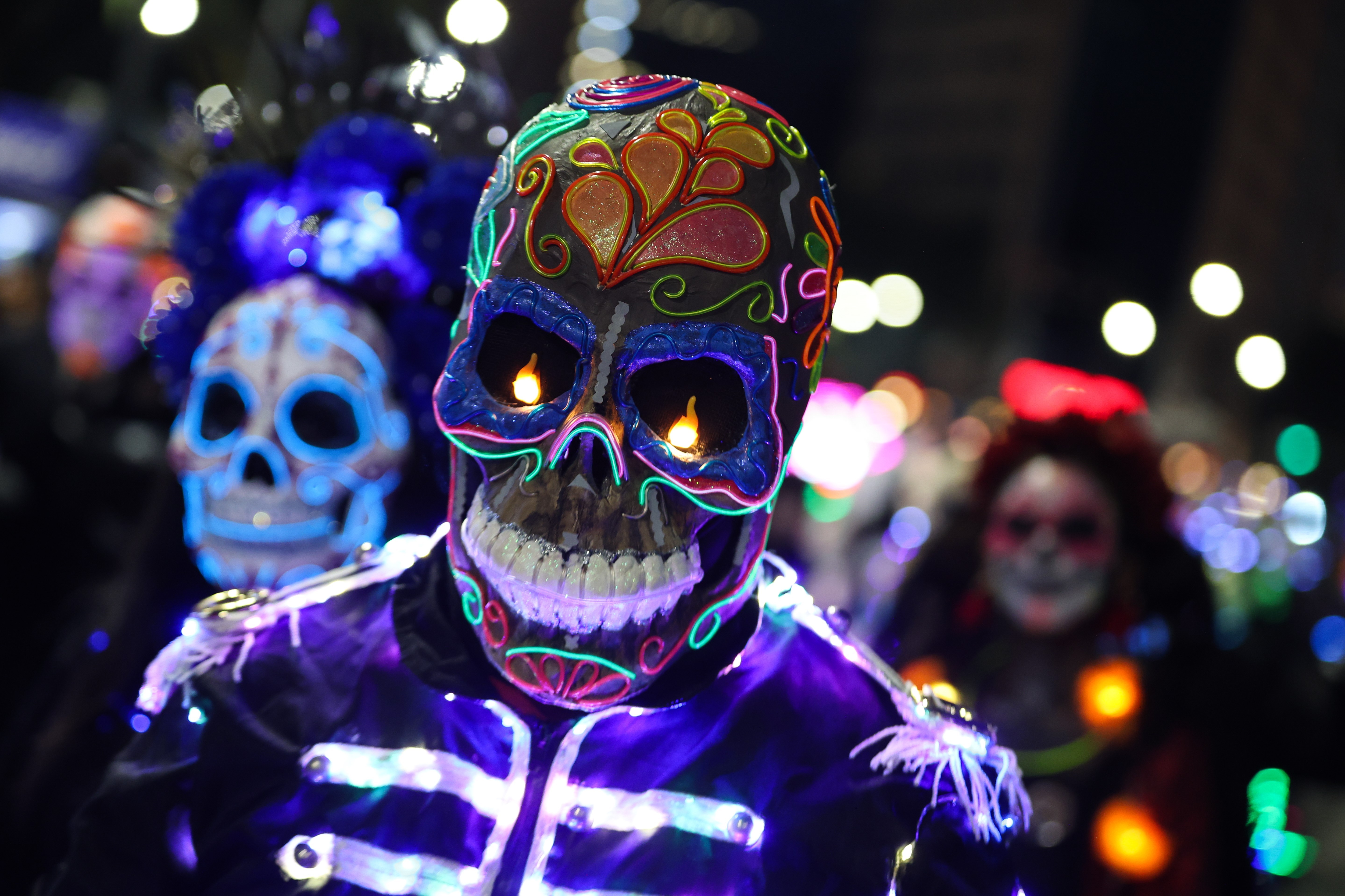 People in colorful skeletal costumes march in a parade.