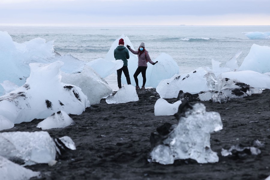 A couple takes pictures on a beach in among icebergs.