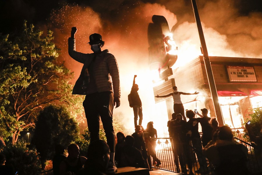 Protesters stand near a burning Arby's restaurant.