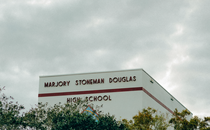 photo of building with "Marjory Stoneman Douglas High School" on it, behind trees against cloudy gray sky