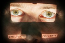 A close-up of a man's face with the eyes illuminated and the words "reject" and "accept" superimposed on his cheeks