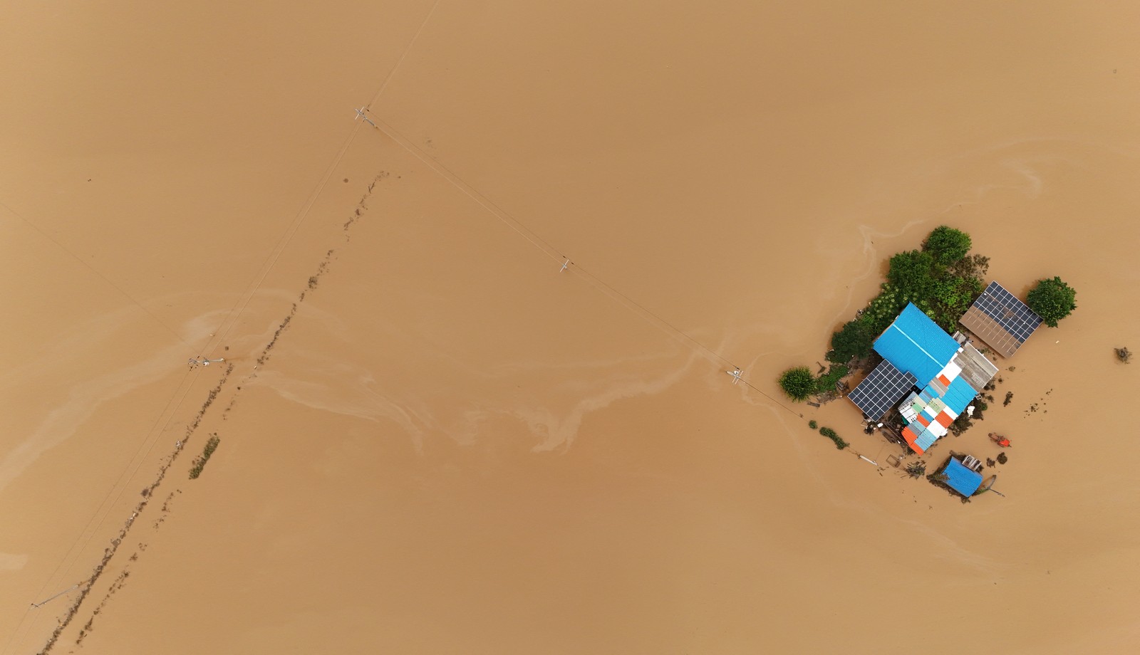 An overhead view of a small house and several small buildings surrounded by floodwater.