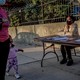 A woman and child walk past a voter-registration table in Brooklyn. Another woman is sitting at the table. Both adults are wearing masks.