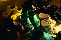 A photograph of eight pairs of yellow, green, and black crocs in an entryway.