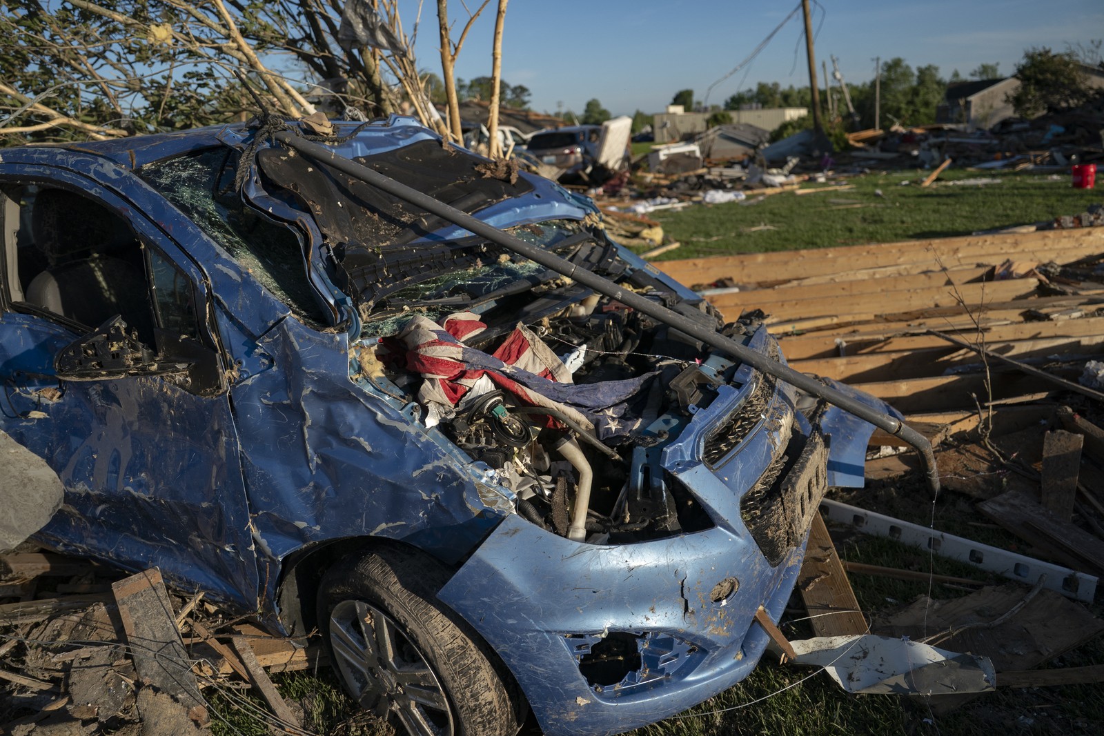 A U.S. flag is seen, twisted in debris on a tornado-damaged car.