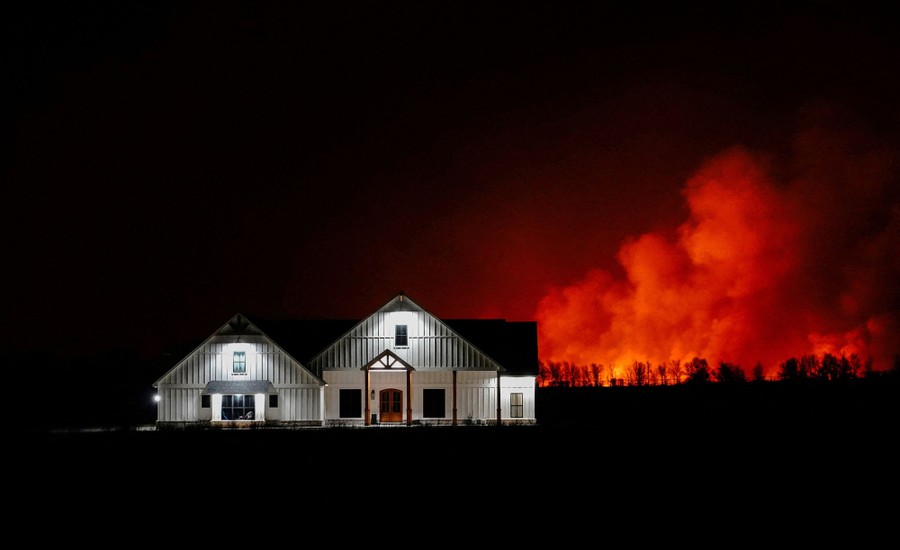 A nighttime view of a ranch house with a forest fire burning in the background