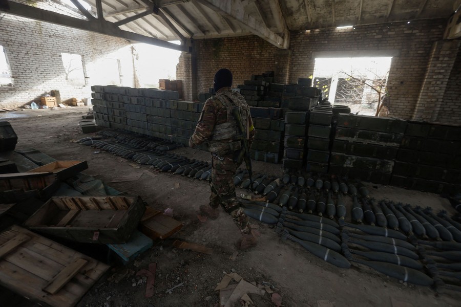 A soldier walks past piles of captured ammunition stored inside an empty building.