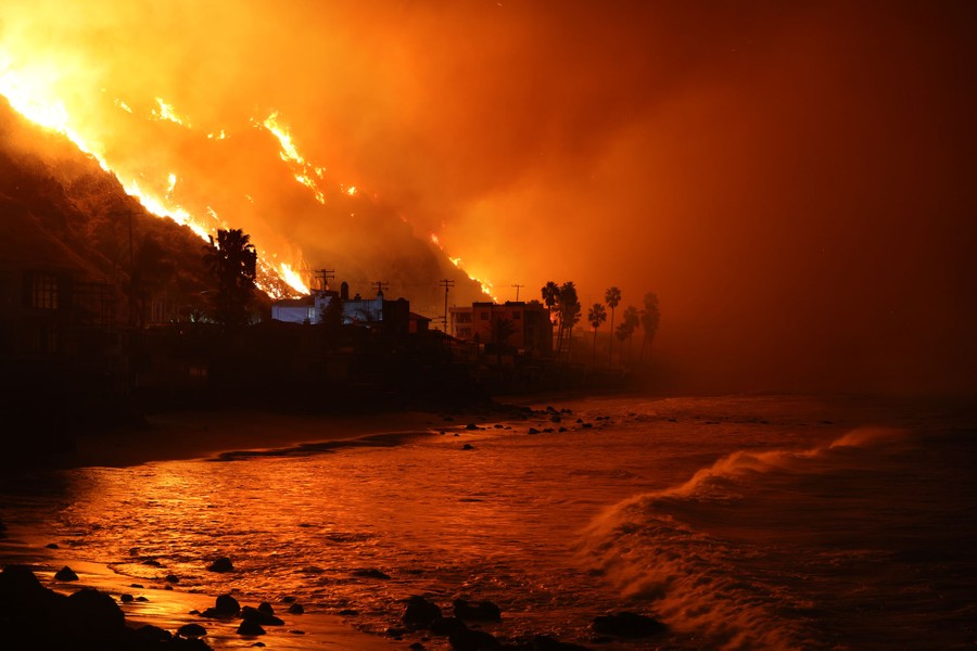 A wildfire burns on hillsides above a beach.