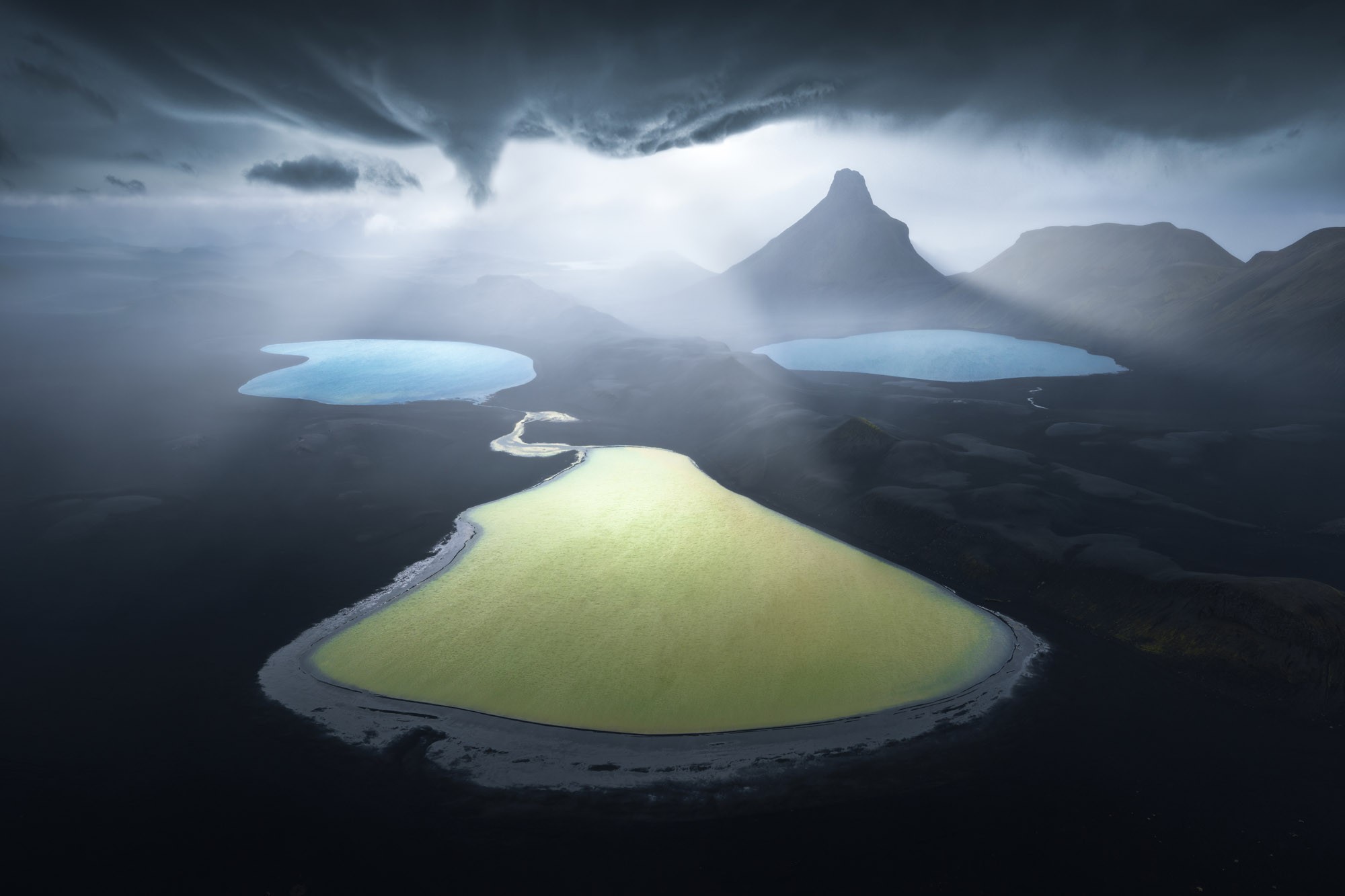 An aerial view of several different-colored lakes in a dark Icelandic landscape