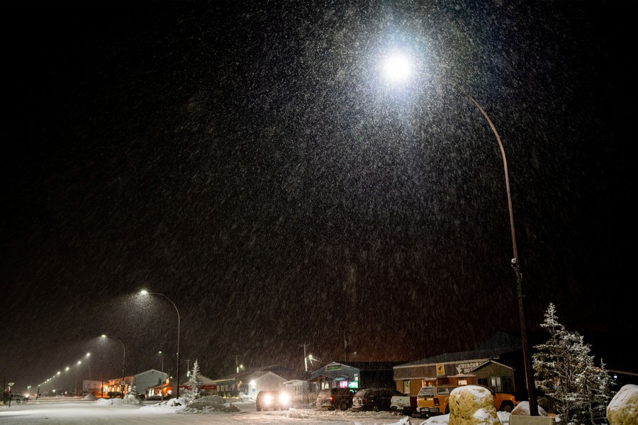 Snow falls over a residential area at night.