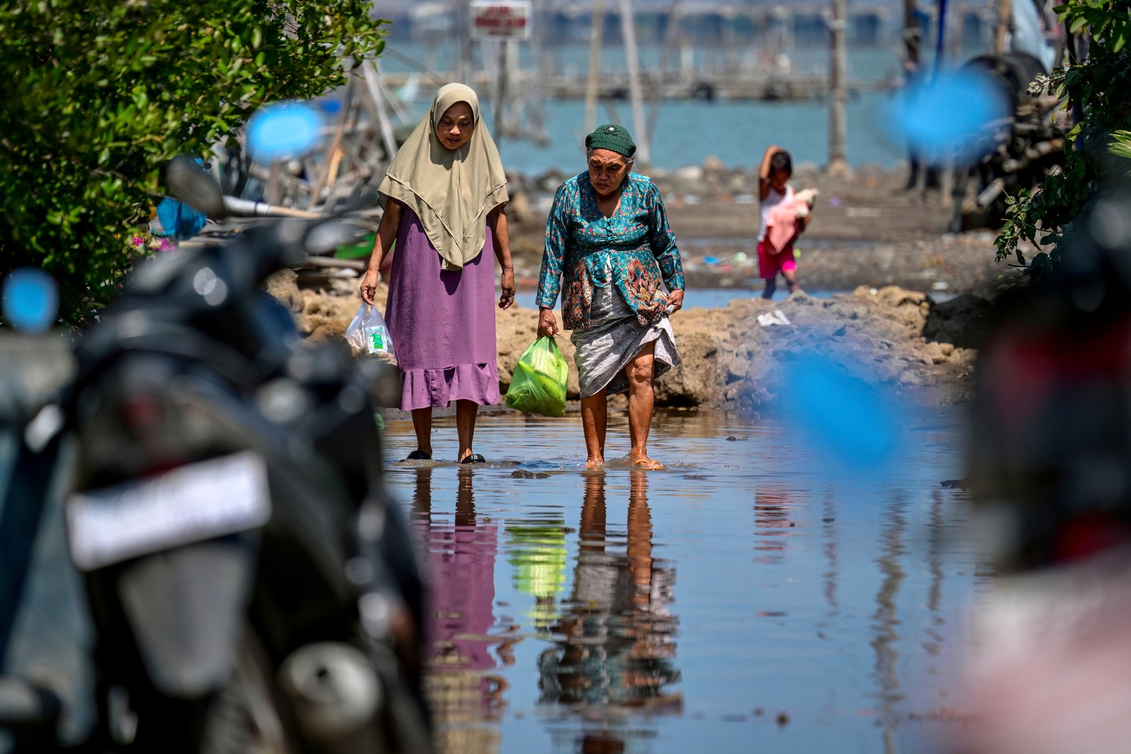 Two people carrying bags walk along a flooded road.