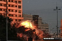 Photograph of flames bursting from an explosion on the side of a building at dusk
