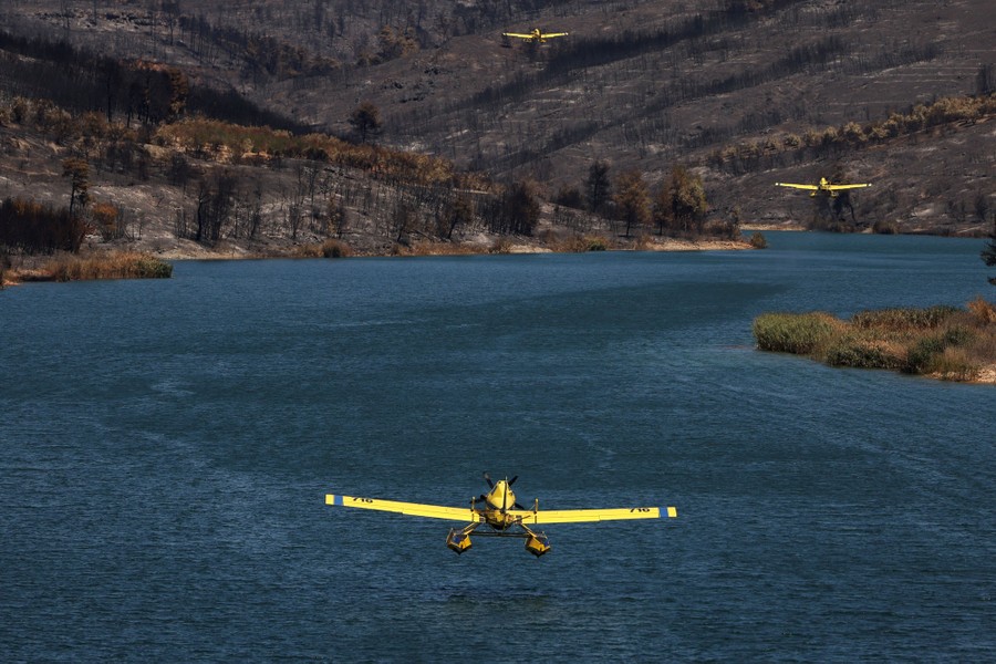 Three small firefighting float planes fly above a lake, beside hills covered with burned trees and brush.