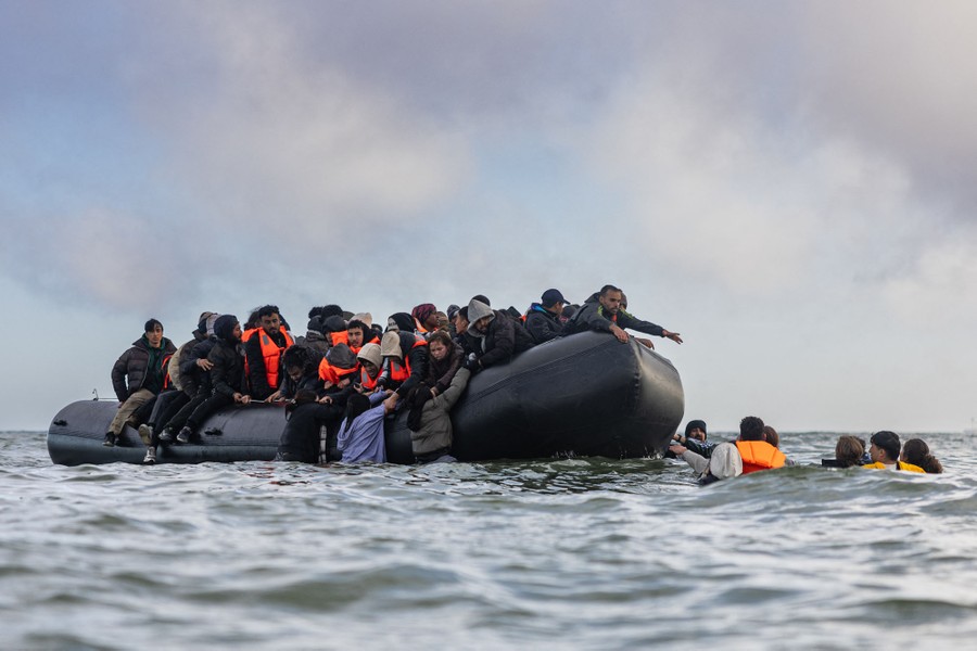 Several people swim toward an inflatable boat that is already overloaded with other people.