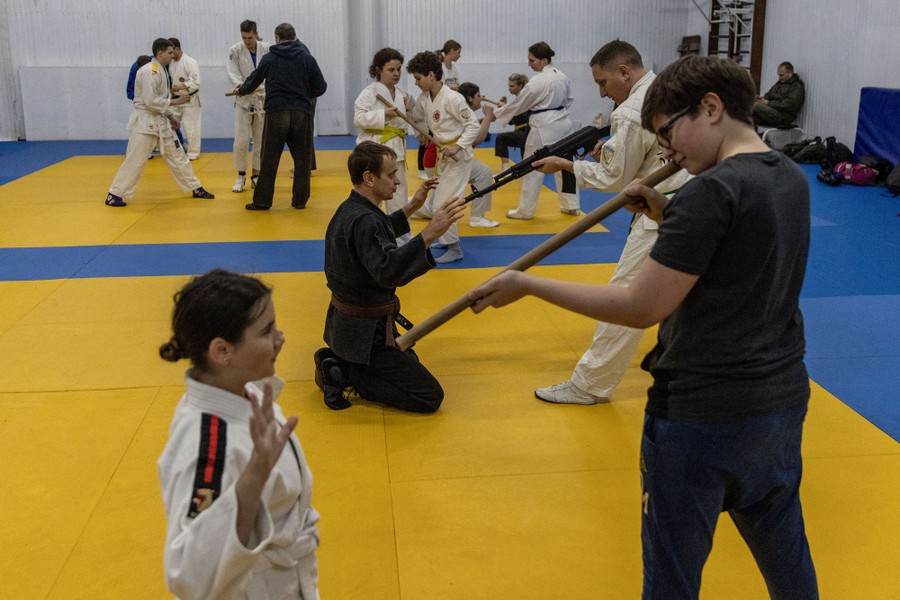 More than a dozen students and instructors train with weapons and replica weapons in a gymnasium.