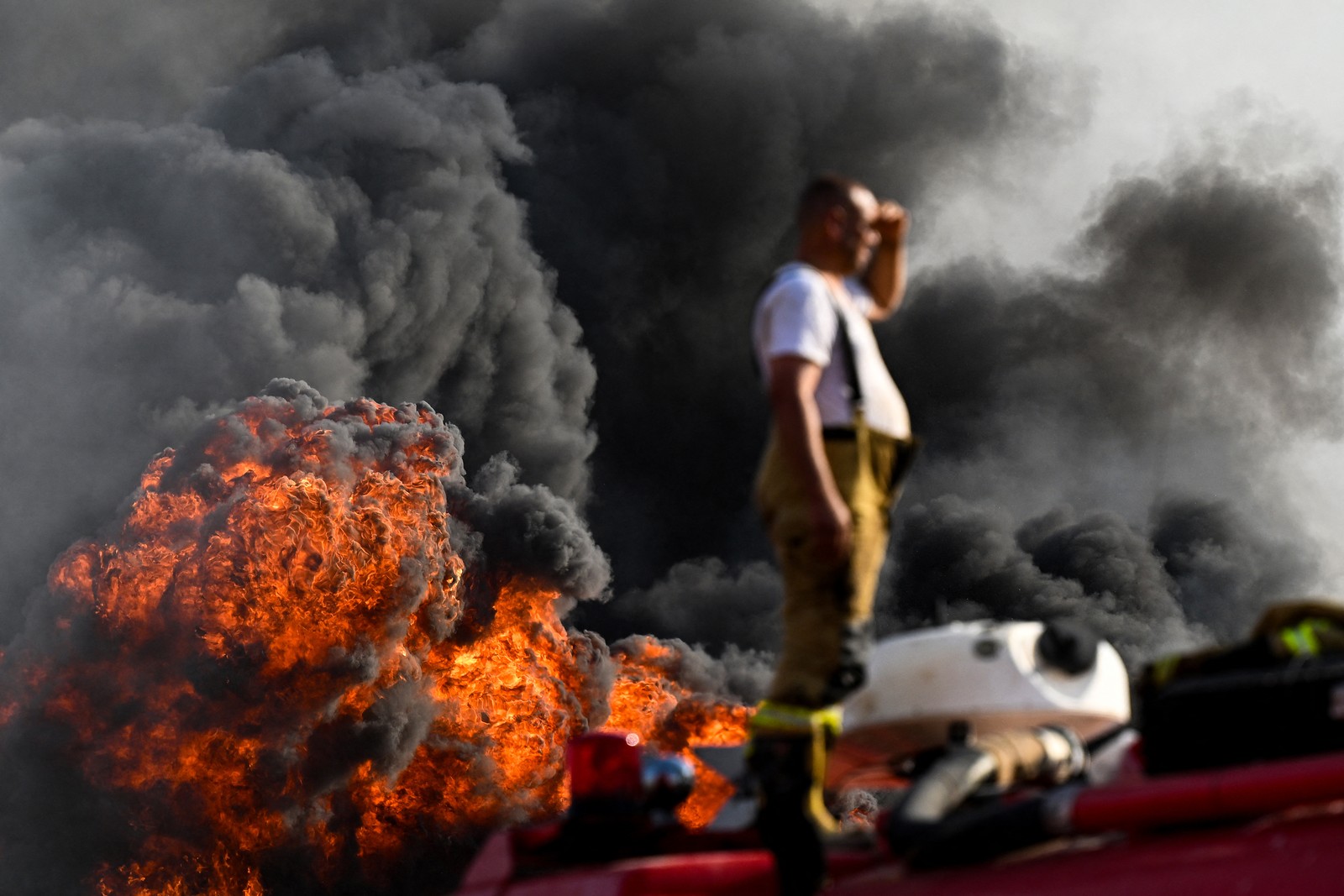 A firefighter looks on as large clouds of smoke and fire billow in the background.