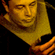Elon Musk looking at a smartphone whose screen lights up his face in pulsating glow