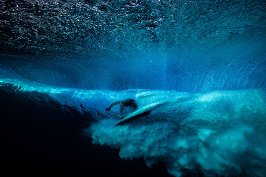 An underwater view of a surfer passing overhead, riding a crashing wave
