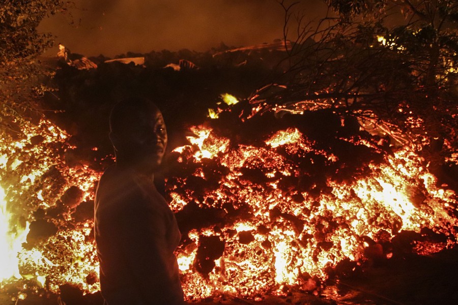 A person stands in front of a wall of glowing lava at night.