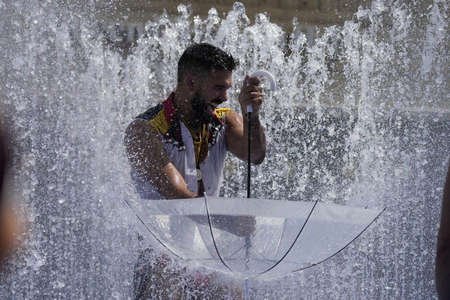 A person plays in a fountain, holding an umbrella upside down.
