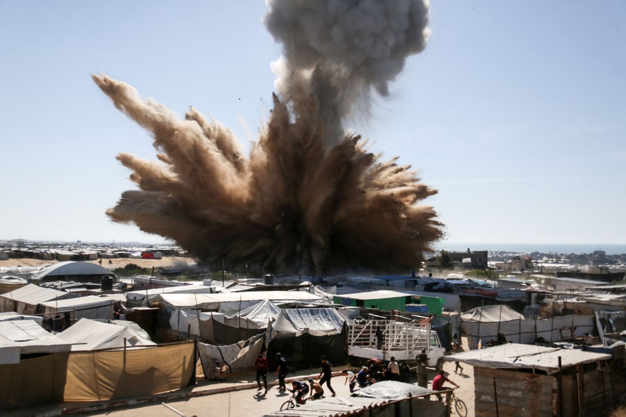 People run for cover as a plume of dirt and smoke rises above tents at a camp for displaced people, following an air strike.