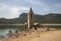 People walk around and look at the ruins of an old church standing in a reservoir with low water.