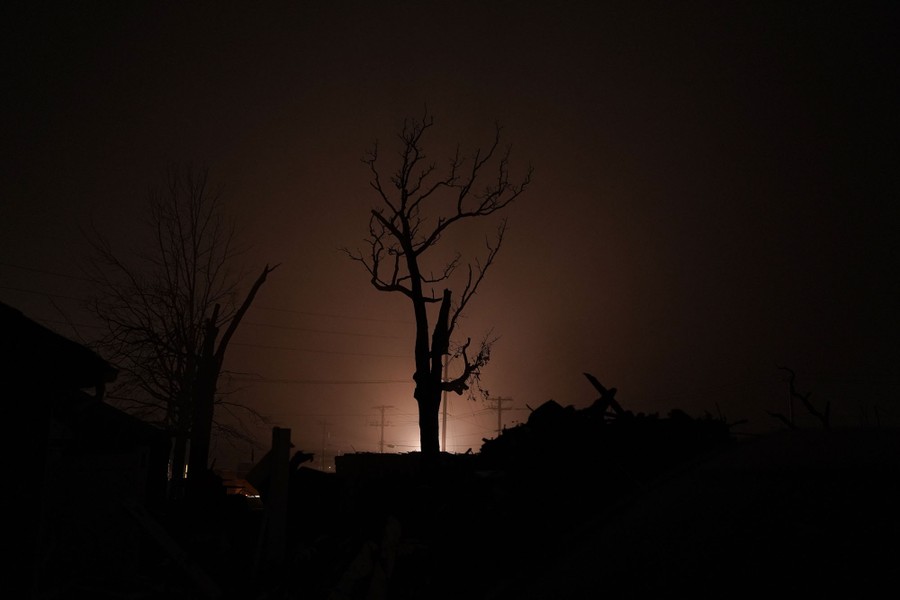 A broken tree stands silhouetted by a single light at night.